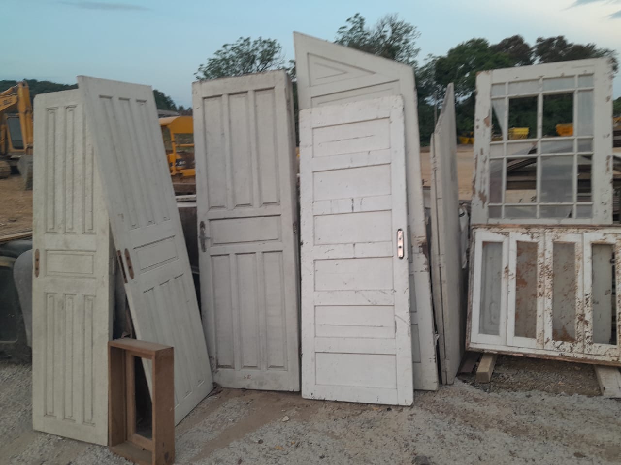 Portas e janelas de demolição dispostas no pátio, evidenciando a variedade de material de construção civil reaproveitado disponível para venda.
