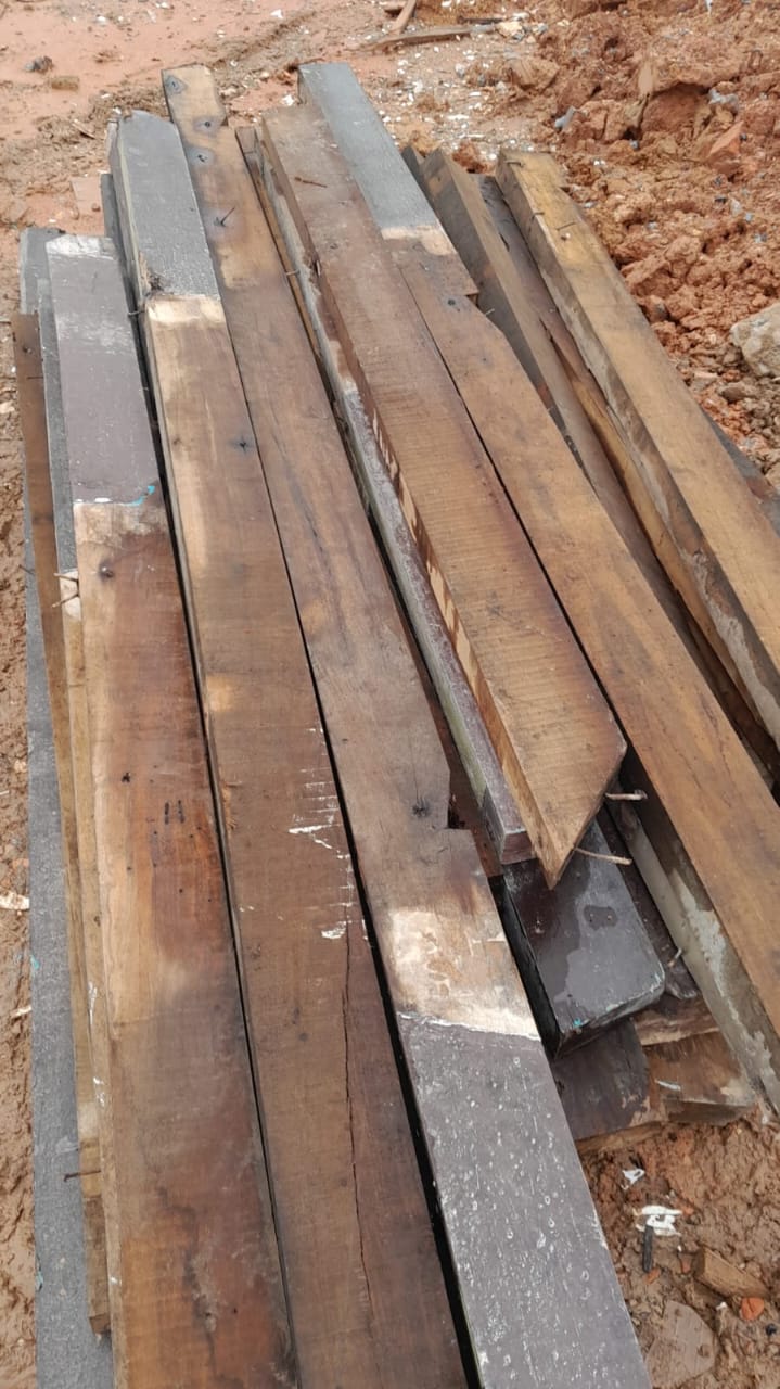 Pilhas de pranchas e vigas de madeira reaproveitada dispostas no chão, mostrando o estoque de material de construção civil para reúso.