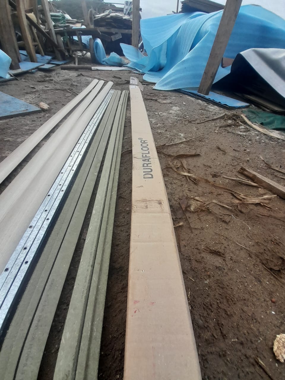 Estoque da Cia das Madeiras com réguas de madeira, perfis metálicos e pacotes de piso Durafloor reutilizados dispostos no pátio de armazenagem.